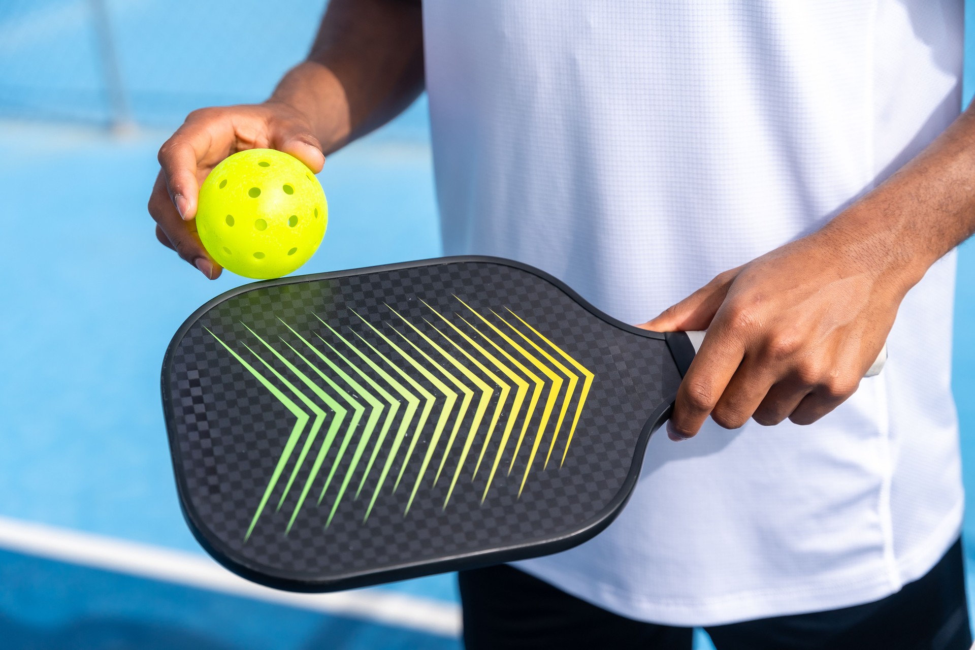 Close-up of a player holding a pickleball paddle and yellow ball